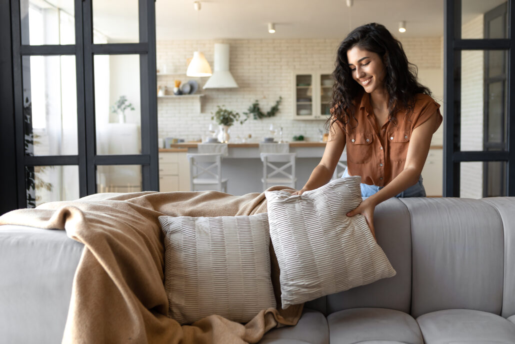 A woman making the sofa tidy with pillows in a modern, bright living room, showcasing professional home cleaning services.