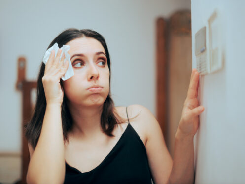 homeowner checking thermostat wiping forehead